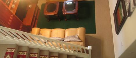 A living room with a sofa, two side tables, a staircase with patterned carpets, and a wooden cabinet.