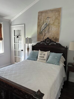 Un dormitorio con cama, una puerta, un cuadro y una mesita de noche.