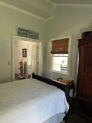Un dormitorio con una cama grande, una ventana con vistas, un aparador de madera y una puerta que conduce a otra habitación.
