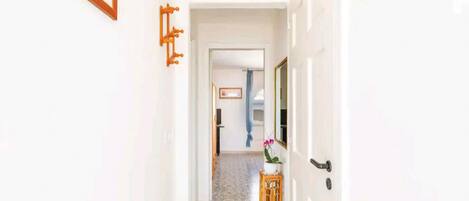A hallway with patterned floor tiles, a wooden side table with a potted plant, and framed pictures on the walls.