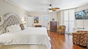 Une chambre avec un grand lit, un ventilateur de plafond, une télévision et un fauteuil à motifs.