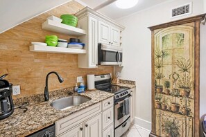 Une cuisine avec des meubles blancs, un plan de travail en granit, un four à micro-ondes, une cuisinière et un évier.