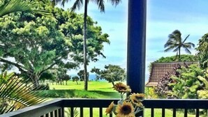 Un balcón con una mesa y sillas, un jarrón con girasoles y vistas a un campo de golf y palmeras.