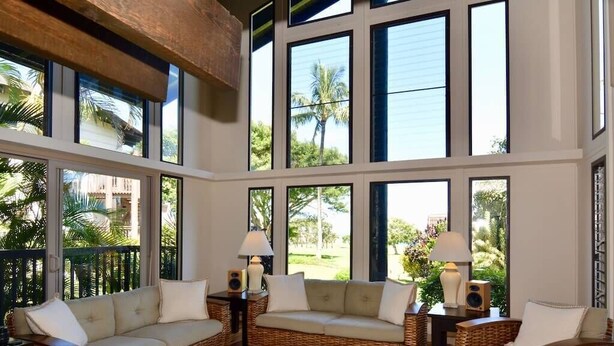 Amplia sala de estar con ventanas grandes, mobiliario de mimbre y vista a palmeras.