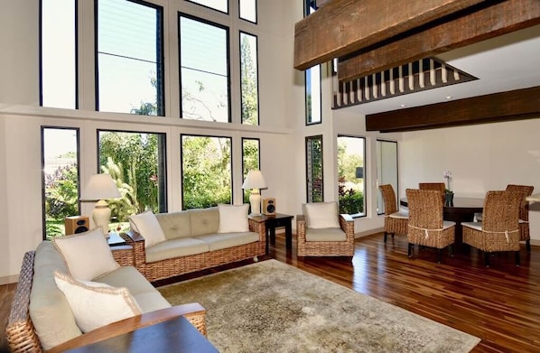 A spacious living room with a large sofa, two armchairs, a coffee table, and a dining area with chairs and a table. - Beautiful Tropical Getaway - Pool - Grill & More (Princeville)