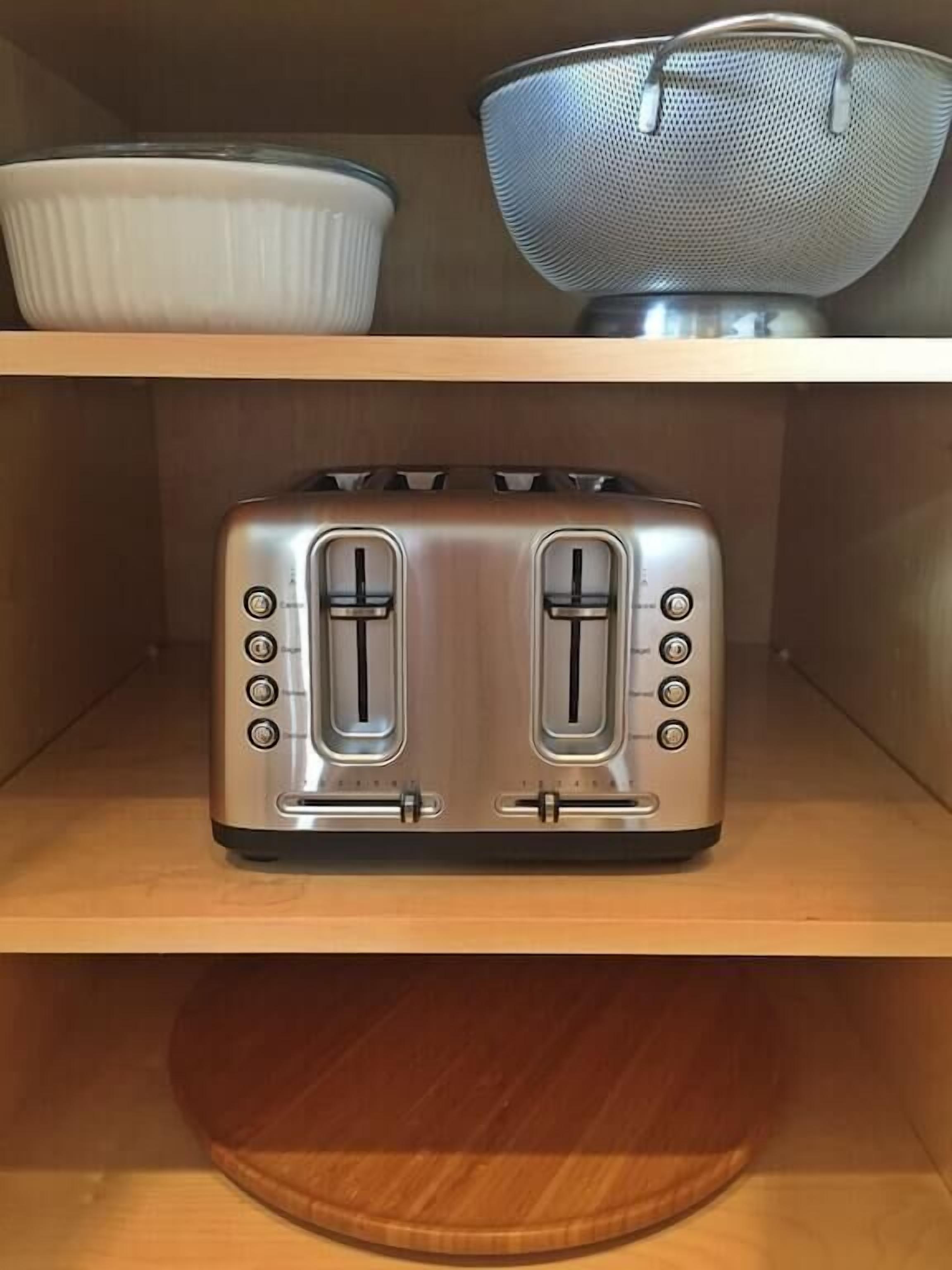 Une cuisine avec un grille-pain en acier inoxydable posé sur une étagère en bois, un saladier blanc et une passoire en métal.