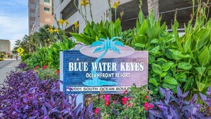 A sign for Blue Water Keyes Oceanfront Resort with a view of the surrounding greenery and a building in the background. - Bluewater Keyes 10th Floor. Oceanfront, Sundeck, Pools | Bluewater Keyes - 1007 (North Myrtle Beach)