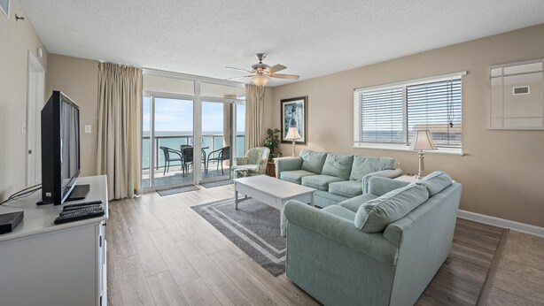 A spacious living room with a large sofa, a coffee table, and a television. There is a balcony with a view of the ocean. - Bluewater Keyes 10th Floor. Oceanfront, Sundeck, Pools | Bluewater Keyes - 1007 (North Myrtle Beach)
