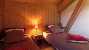 A cozy room with wooden walls and a sloped ceiling, featuring two beds with pillows and a nightstand with a lamp. - COEUR DES ALPES - Sabot de Vénus (Taninges)