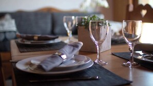 A dining table set with plates, cutlery, and wine glasses, with a sofa and a plant in the background. - COEUR DES ALPES - Sabot de Vénus (Taninges)