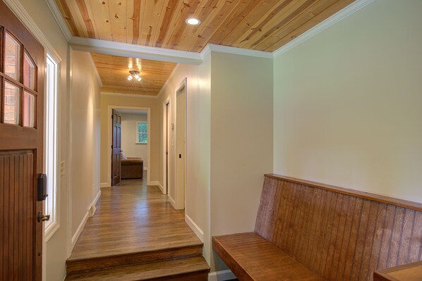 A hallway with wooden flooring, a bench, and a door with a light switch.