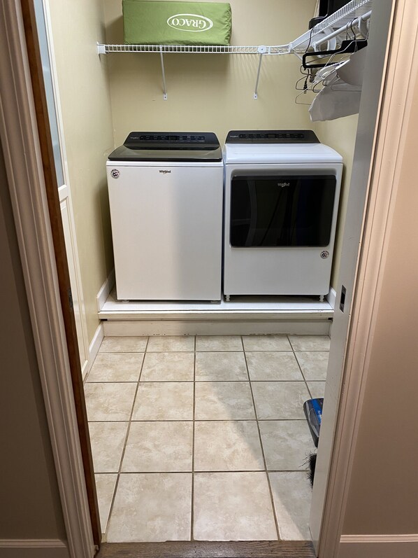 A laundry room with a compact washer and dryer, a drying rack, and a green towel hanging above. - Spacious, In-Town Hideaway (Highlands)