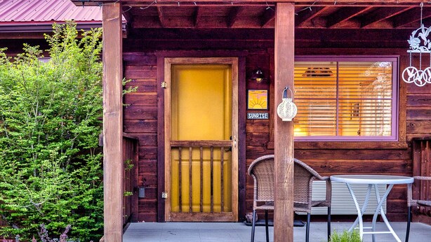 A wooden cabin with a yellow door, a porch with chairs, and a sign that reads "SUNRISE". - The Loubird Inn (Escalante)