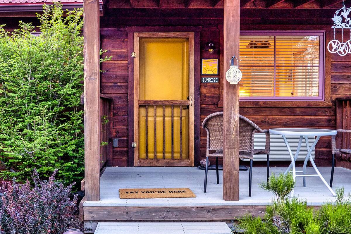 A wooden cabin with a yellow door, a porch with chairs, and a sign that reads "SUNRISE".