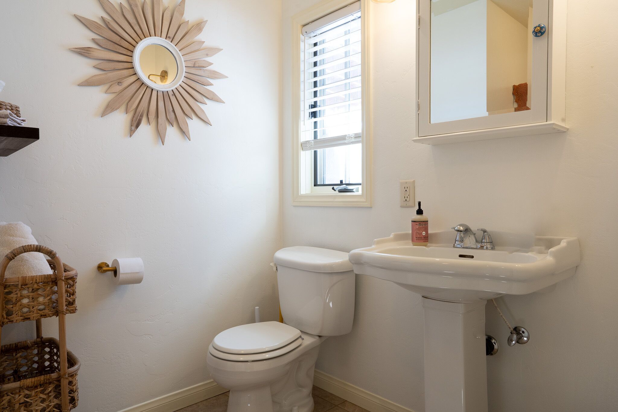 A bathroom with a toilet, sink, and a decorative sunburst mirror.