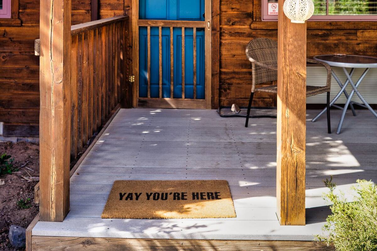 A wooden cabin with a blue door, a doormat with text, and a sign that says "RIVER".