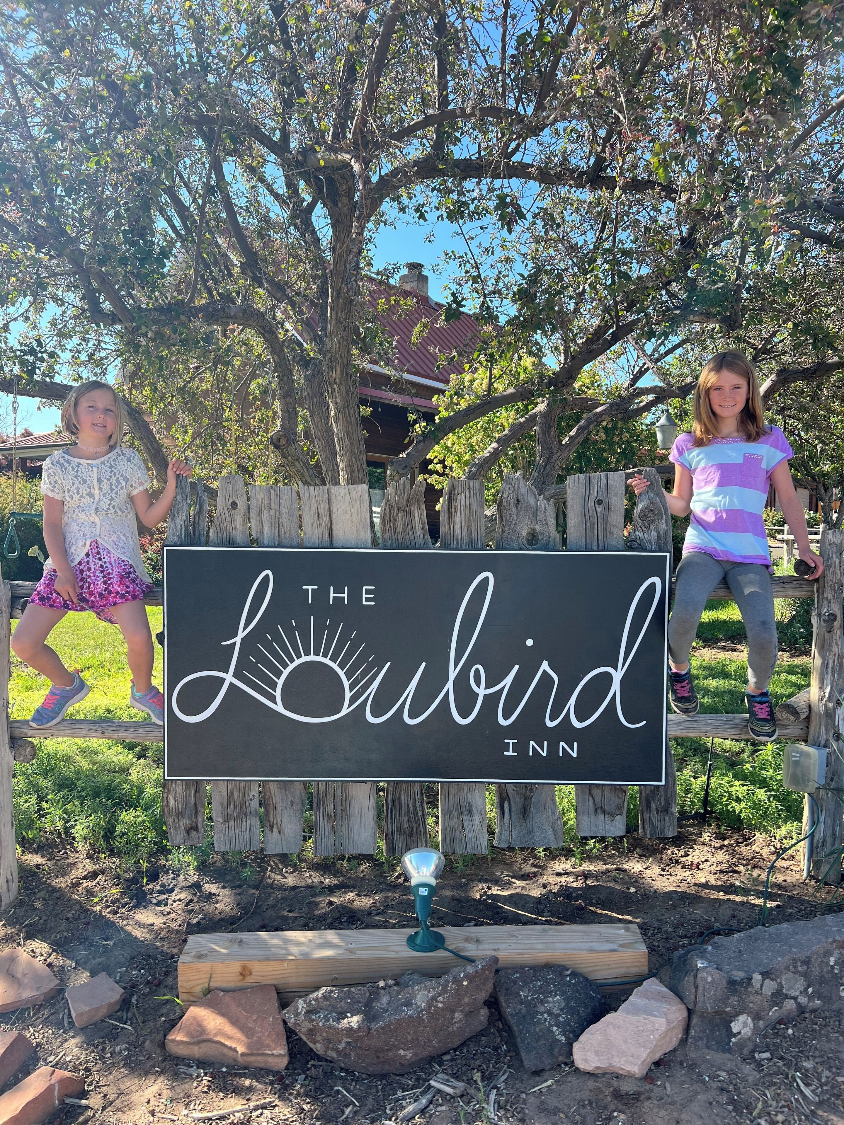 A sign for The Lubbird Inn with a rustic wooden fence and a clear sky in the background.