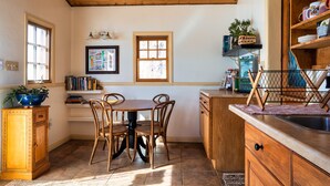 A kitchen with wooden cabinets, a dining table with chairs, and a window with blinds. - The Loubird Inn (Escalante)