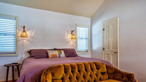 A bedroom with a large bed, two wall-mounted lamps, a door, and a small side table. - The Loubird Inn (Escalante)
