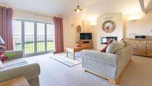 A living room with a sofa, a coffee table, a TV, and a kitchen area with cabinets and a microwave. - 🌿 Welcome to Tylney Retreat – Your Breathtaking Cornish Hideaway 🌿 (Edmonton)