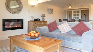 A living room with a fireplace, a sofa, a coffee table with fruit, and a mirror on the wall. - 🌿 Welcome to Tylney Retreat – Your Breathtaking Cornish Hideaway 🌿 (Edmonton)
