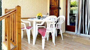 A patio with a wooden staircase, white plastic chairs, a small table with a vase of flowers, and a wooden door. - Cozy House with Pool & Tennis, Near Beach, Sleeps 6 - Bormes-les-Mimosas (Bormes-les-Mimosas)