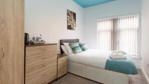 A bedroom with a bed, a wardrobe, a bedside table, a window with blinds, and a ceiling light. - Townhouse @ Westminster St (Crewe)