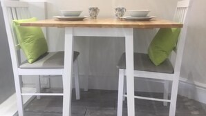 A small dining table with two chairs, each with a green cushion. - Townhouse @ Westminster St (Crewe)