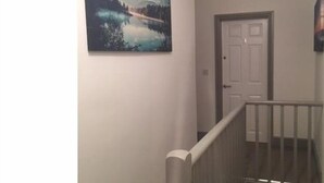 A hallway with a wooden railing, a door, and a painting of a landscape. - Townhouse @ Westminster St (Crewe)