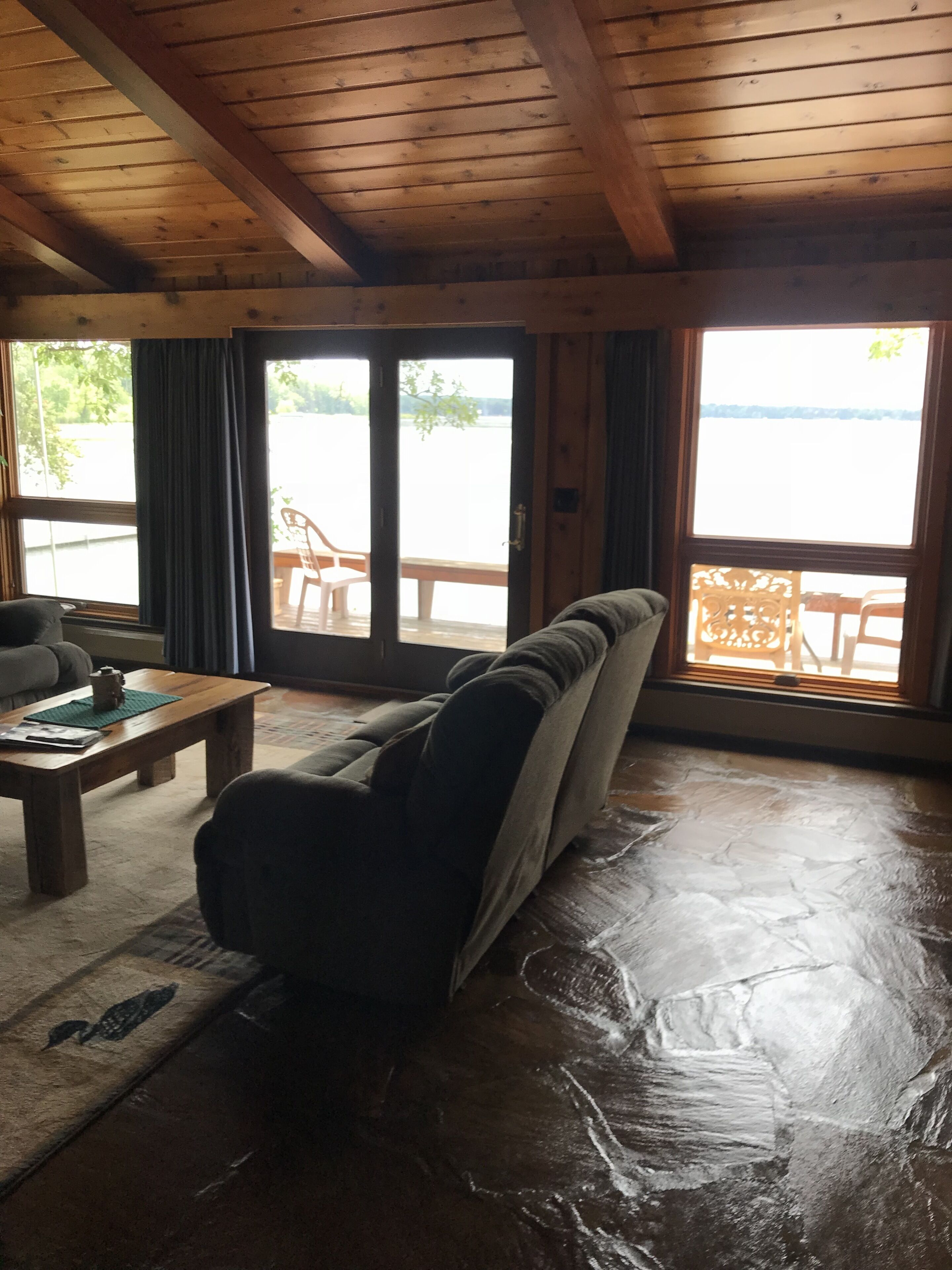 A cozy living room with a sofa, a coffee table, and a view of a lake through large windows.
