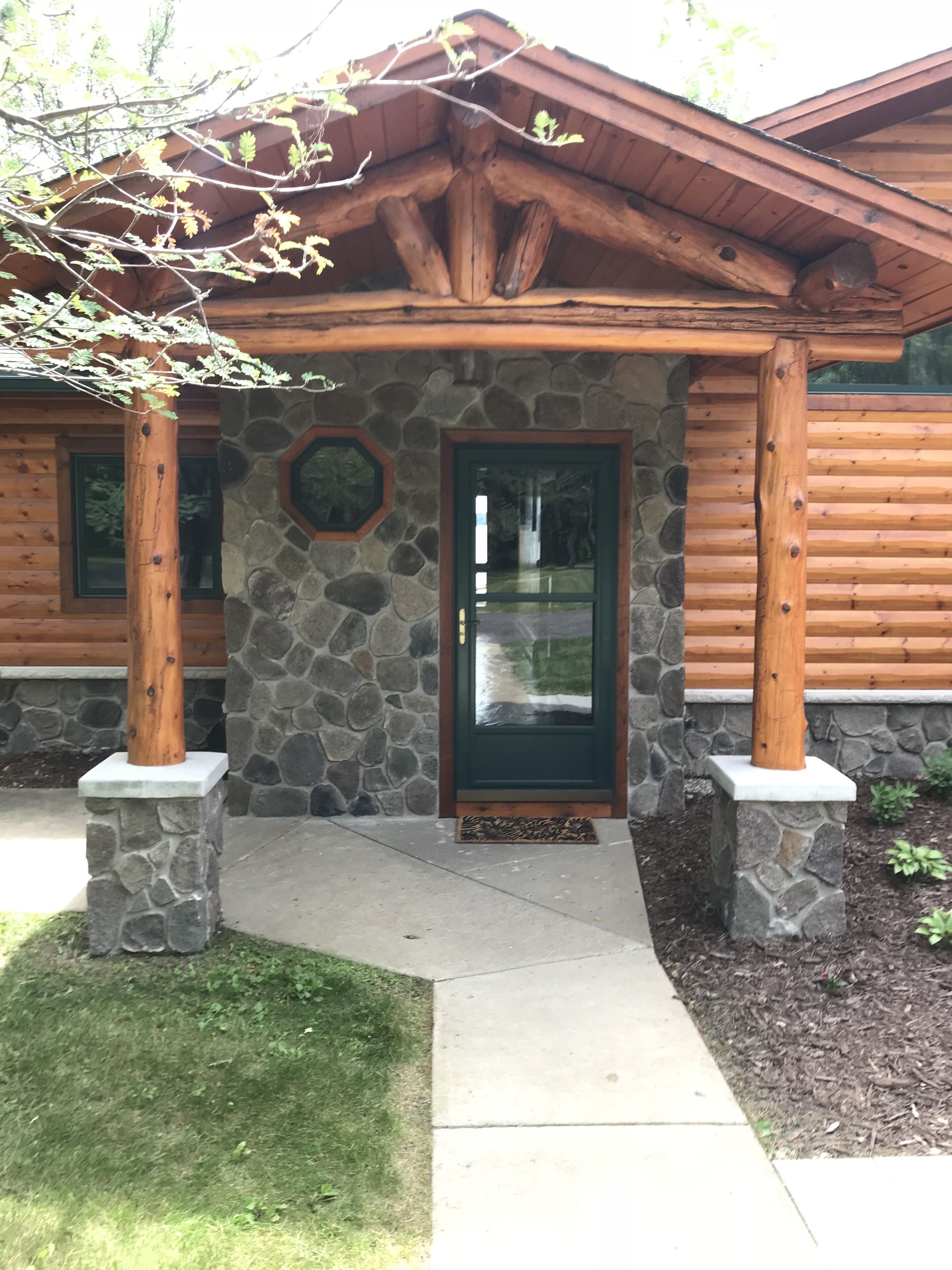 A log cabin with a stone foundation, a green door, and a stone-framed window.