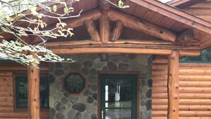 A log cabin with a stone foundation, a green door, and a stone-framed window.