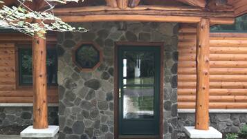 A log cabin with a stone foundation, a green door, and a stone-framed window.