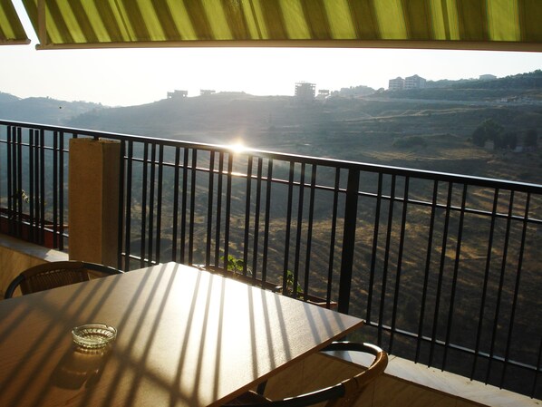 A balcony with a table and chairs, overlooking a hilly landscape with buildings in the distance. - Al Sakhra Hotel (Bhamdoun)