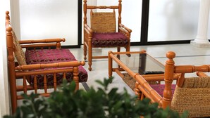 A room with two wooden chairs with woven backs and cushioned seats, a glass coffee table, and a small woven basket. - Al Sakhra Hotel (Bhamdoun)