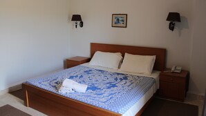 A bedroom with a wooden bed, white pillows, a blue patterned bedspread, two bedside tables with lamps, a framed picture on the wall, and a phone on one of the tables. - Al Sakhra Hotel (Bhamdoun)