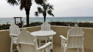 Eine Terrasse direkt am Strand mit weißen Adirondack-Stühlen und einem Tisch, mit Blick auf den Ozean.