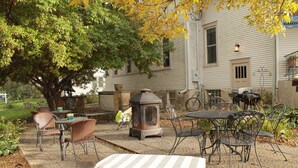 A patio with outdoor furniture, a stone fireplace, and a tree providing shade.