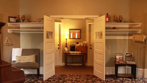 A room with a floral carpet, a piano, a bench with cushions, and a table with a lamp and a welcome sign.