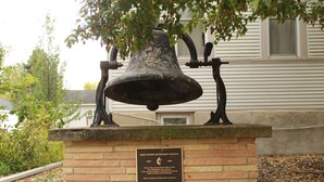 A historical bell mounted on a brick pedestal with a plaque.