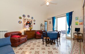 A living room with a brown leather sofa, a blue sofa, a wooden dining table with chairs, and a ceiling fan. - Terrazza Lara (Cefalù)