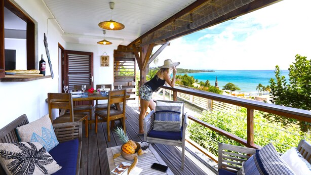 Un terrazza in legno con zona pranzo, un tavolo apparecchiato con bicchieri da vino e vista sull'oceano.