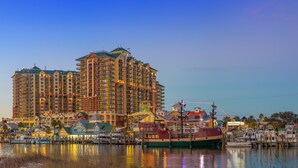 A waterfront hotel with multiple balconies, a marina with boats, and a prominent lighthouse in the background. - Emerald Grande🐠🐠Corner Unit ⛵️ Incredible Gulf Views⛱️Beach Serv Incl 🩴Ev Chargers (Destin)