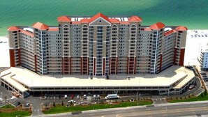 Een hotel met meerdere verdiepingen en een centraal atrium, omringd door parkeergelegenheid en uitzicht op zee.