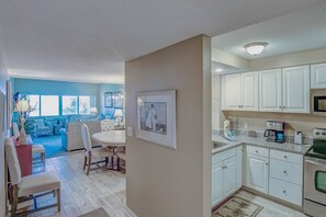 A modern kitchen with white cabinets, a microwave, and a stove. There is a dining area with a round table and chairs. - 464 Captains Walk - 2 bedroom, 2 bath villa convenient to the beach! (Hilton Head Island)