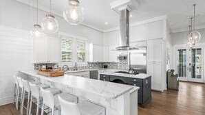 Una cocina moderna con armarios blancos, una isla de mármol y taburetes de bar.