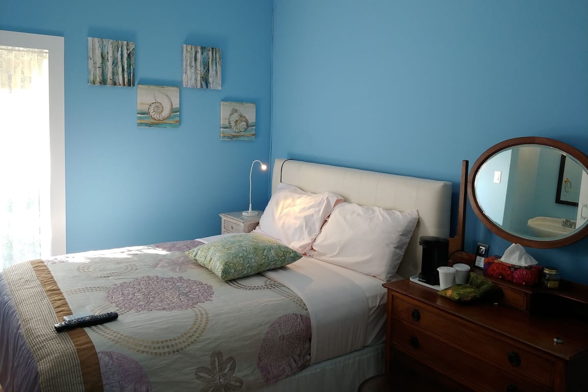 A bedroom with a bed, bedside table, and a dresser. There are wall art pieces above the bed and a mirror on the dresser.