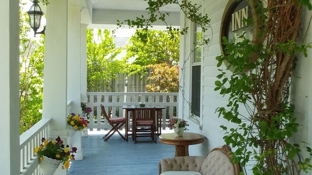 A covered porch with a white fence, a wooden table with chairs, and a bench.