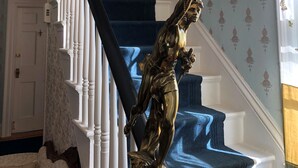 A staircase with white balusters, a blue carpeted landing, and a wall with floral wallpaper.