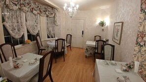 A dining area with floral curtains, wooden chairs, and a chandelier. - Inn on Frederick (St. Andrews)